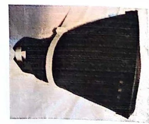 Black cone-shaped fabric cover with a pale cable tie wrapped around its narrow end, on a light surface.